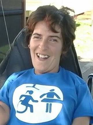 Foto de Marian. Tiene el pelo corto, está sentada en su silla de ruedas y lleva puesto una camiseta con el logo de la Asociación Cambiadores Inclusivos.
