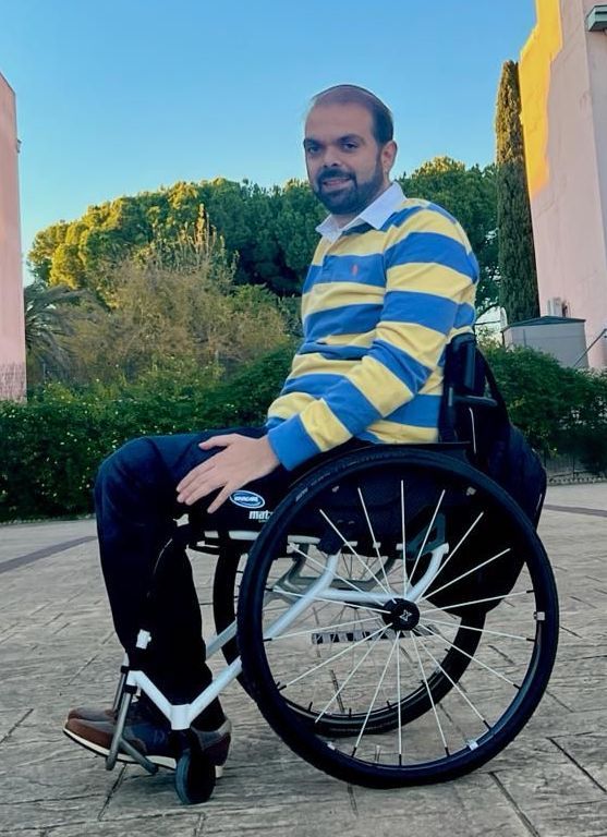 Foto de Francisco Zuasti en su silla de ruedas. Está en una plaza, lleva un polo, pantalones de sport y una mochila colgada del respaldo de la silla